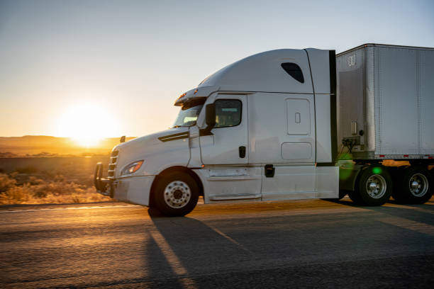 long haul semi-truck rolling down a four-lane highway at dusk - four lane highway stock-fotos und bilder