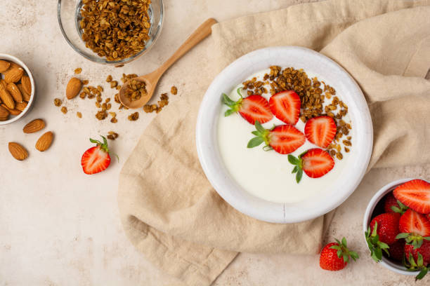 istock Greek yogurt in white bowl with ingredients for making breakfast granola and fresh strawberries on old beige table. Top view. 1299976952