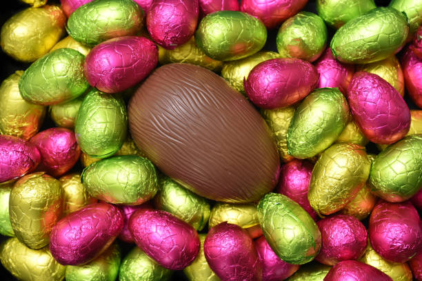 istock Pile or group of multi colored and different sizes of colourful foil wrapped chocolate easter eggs in pink, red, yellow and lime green with a large brown milk chocolate egg in the middle. 1299977480
