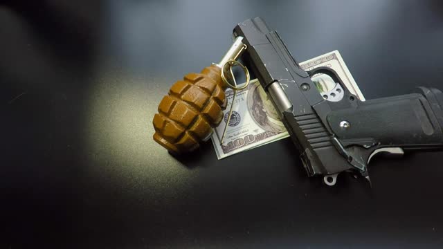 gun money and hand grenade close up on a black table