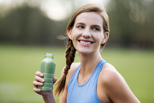 Head and shoulders side view of Caucasian woman in late 20s wearing sports bra and looking away from camera while holding refreshment after workout.