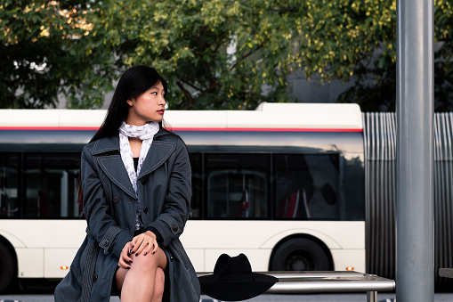 asian woman sitting and waiting for the bus al the bus stop, concept of public transportation and urban lifestyle
