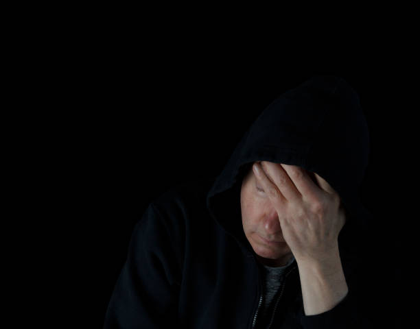 istock Depressed mature man holding his forehead while wearing a hooded sweater in the dark 1299982755