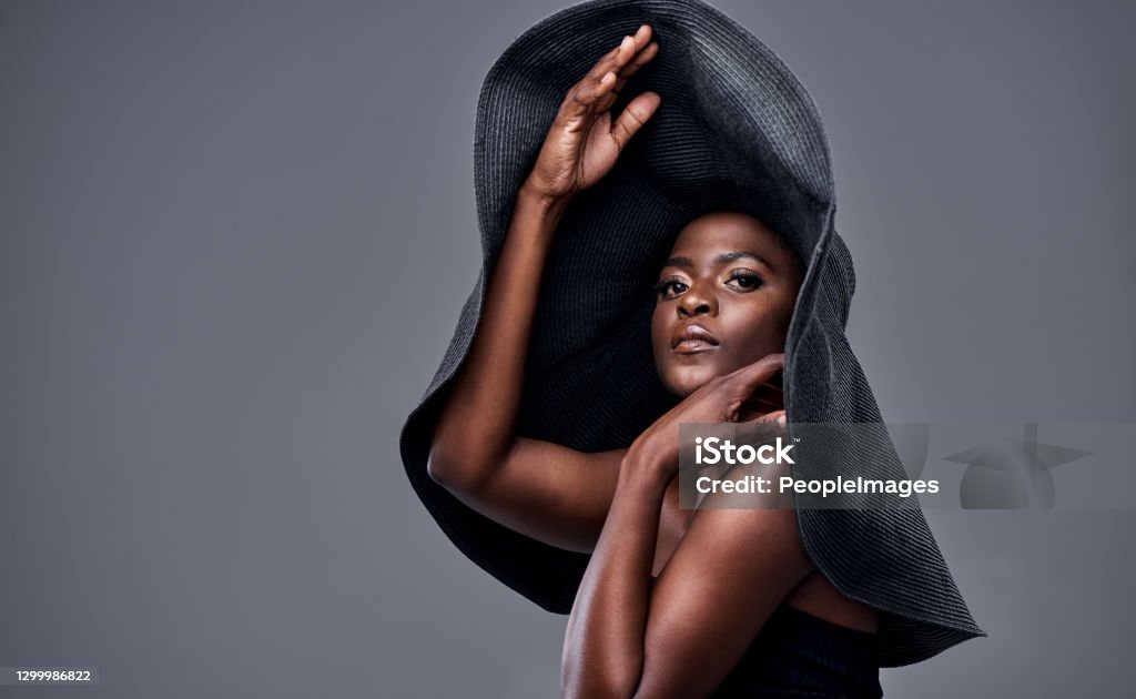 The bigger the hat, the bigger the dreams Shot of a young woman wearing a oversized sunhat against a grey background Haute Couture Stock Photo
