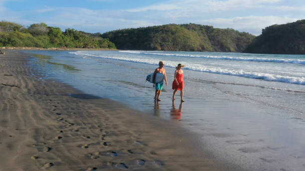 istock Mature couple walk down beach before morning surf session 1299988888