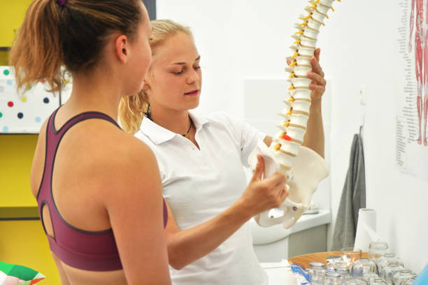 istock Young woman patient at physiotherapy consultation, therapist explaining her back bones on spine model 1299990544
