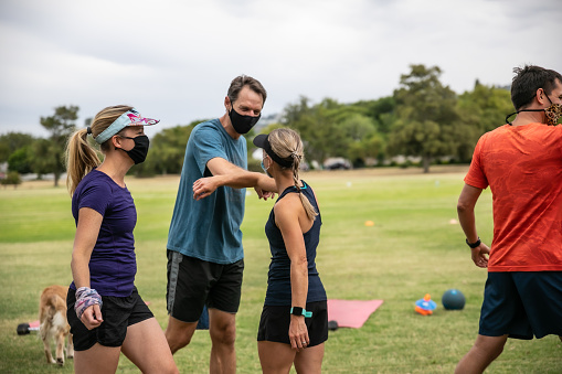 A group of people meeting for an outdoor training session. They are greeting each other with the elbow and are wearing masks.
