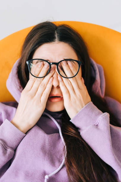 junge frau reibt sich die augen, nachdem sie eine brille vor dem laptop benutzt hat. augenschmerzen oder müdigkeit konzept... - human eye rubbing tired glasses stock-fotos und bilder