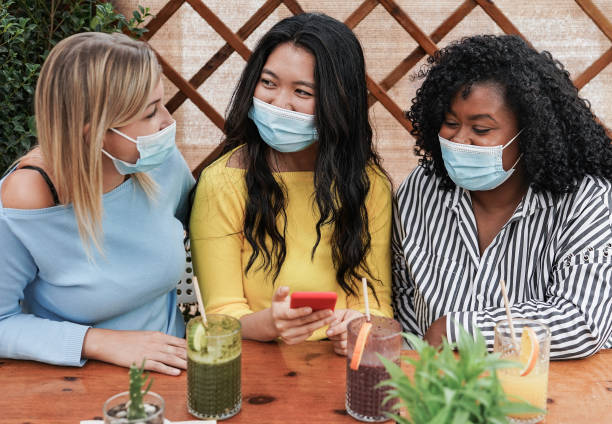 istock Cheerful multiracial women looking at smartphone and smile while wearing protective face masks for coronavirus outbreak 1299993166