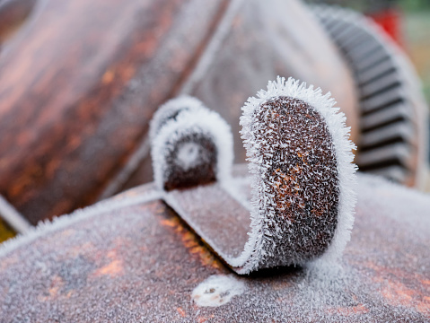 Macro view of a piece of metal on top of the metal casing of the motor of a concrete mixer completely frozen by the rime produced by fog during winter