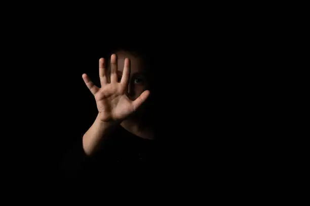 Photo of little girl with a raised hand making a stop sign gesture on a black background.