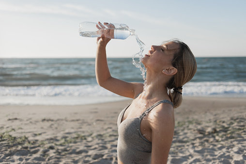 beautiful young woman drinks water after a workout. Tired pours liquid on itself. Hot. Quench your thirst. Ocean. Place for text