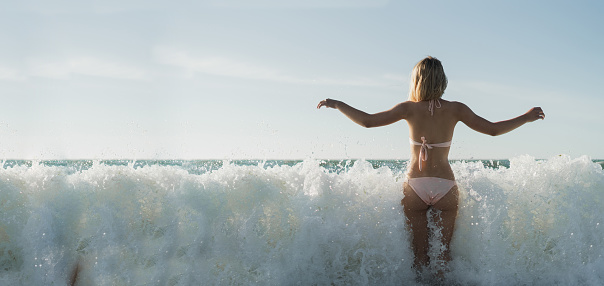 young girl during a hot summer day jumps in the sea waves. Back view. Travel, active, yoga, lifestyle freedom concept. Vacation on the ocean. Place for text. Copy space