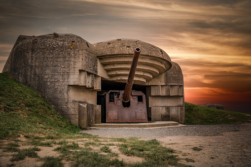 Atlantic wall concrete German World War Two gun emplacement fortification bunker battery at Longues-sur-mer in Normandy Gold Beach France remains lay in ruins with beautiful orange sunset sky