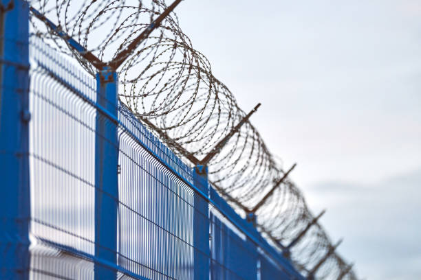 istock Barbed wire on blue fence of restricted area 1300002968