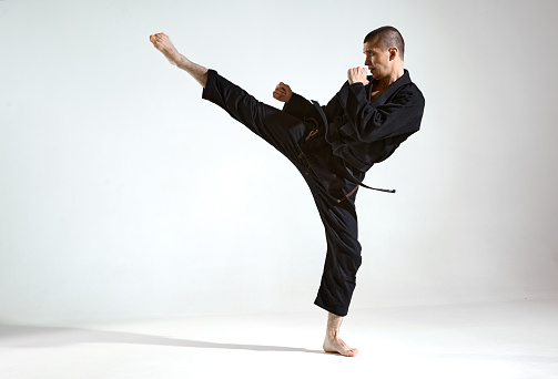 Fighting guy in black kimono fighter shows kudo technique on studio background with copy space, mix fight concept. High quality photo