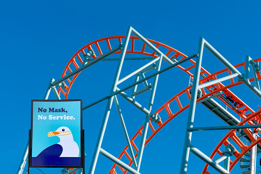 Santa Cruz, California, USA - January 18, 2021: Roller coaster at Santa Cruz, California, beach boardwalk with sign requiring masks. Rides remain closed due to COVID virus restrictions.