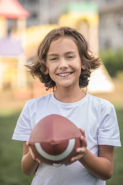 istock Dark-haired boy in a white tshirt holding a ball and smiling 1300008944