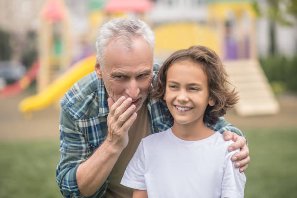 istock Gray-haired dad whispering something on his sons ear 1300009050