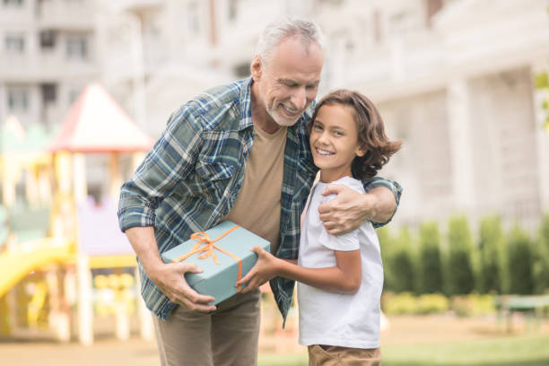 istock Gray-haired man holding a gift box and hugging his son 1300009109