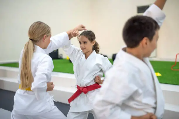 Caucasian teenage kids in kimono practicing karate sparing combat and self defense techniques in a sports gym. Martial arts sport training session for a healthy growth and child development
