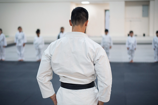Male karate instructor in kimono over viewing the karate training session in a sports gym. Martial arts sport training session for a healthy growth and child development