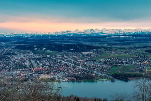 view at the beginning of dusk from the municipality of Magglingen above the city of Biel Bienne over the urban area, the flatlands of the canton of Bern to the swiss alps. in the foreground the lake biel and the aare river