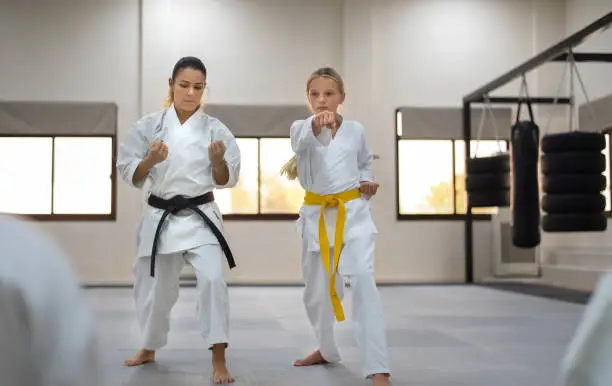Caucasian teenage girl in kimono with yellow belt practicing karate with a karate instructor in a sports gym. Martial arts sport training session for a healthy growth and child development-