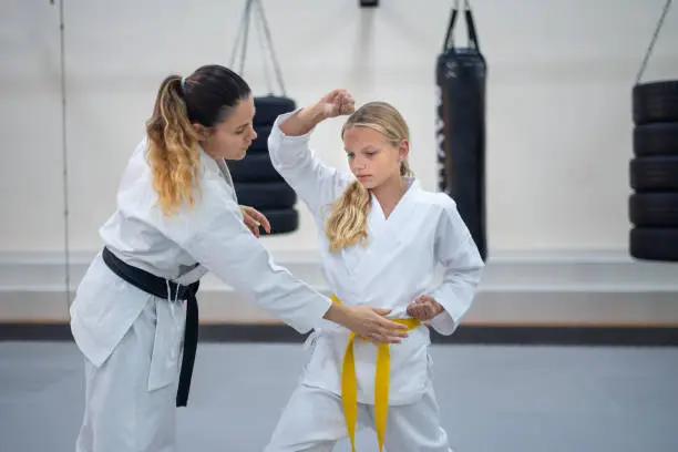 Caucasian teenage girl in kimono practicing karate with a karate instructor in a sports gym. Martial arts sport training session for a healthy growth and child development-