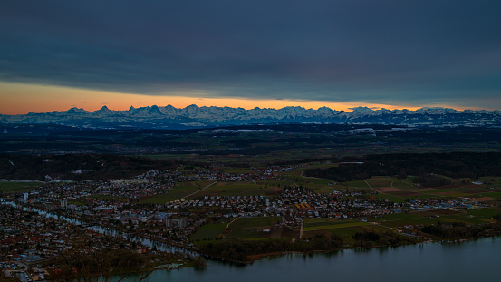 view at the beginning of dusk from the municipality of Magglingen above the city of Biel Bienne over the urban area, the flatlands of the canton of Bern to the swiss alps. in the foreground the lake biel and the aare river