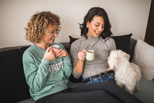 Cute lesbian family enjoying their coffee while small white dog is looking at them curiously.