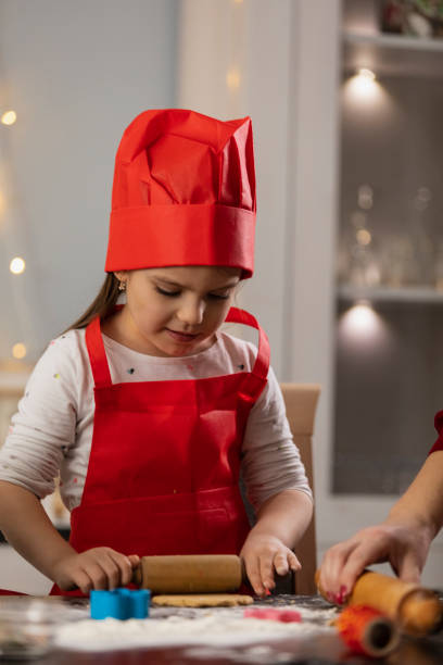 istock Little girl in chef's hat rolling out cookie dough 1300011638