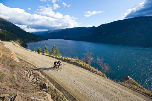 Two men go for a gravel road bicycle ride in British Columbia, Canada. Gravel road bicycles are similar to cyclocross bikes with disc brakes and oversized tires for riding on rough terrain. They both wear cycling helmets and cold-weather cycling clothing. They carry tools, food, and extra clothing in bags strapped to their bikes.