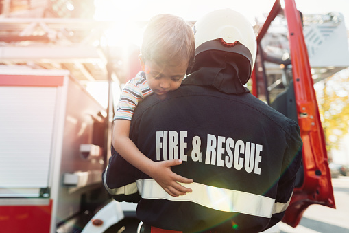 Close-up image of firefighter carrying unconscious little boy to the fire truck cabin
