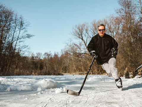Mature man practising hockey outdoors. Exterior of public park with frozen pond.