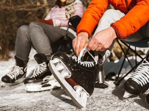 Feet and hands of Mature couple getting ready for ice skating outdoors. Exterior of frozen pond in public park.