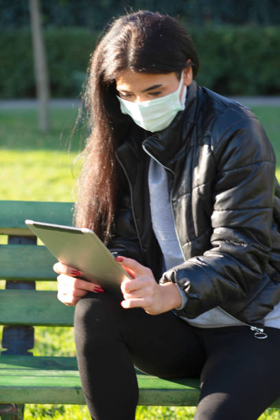 istock Young woman sitting on a bench in a public park using digital tablet 1300016874