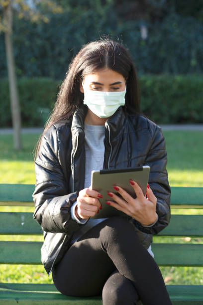 istock Young woman sitting on a bench in a public park using digital tablet 1300017711
