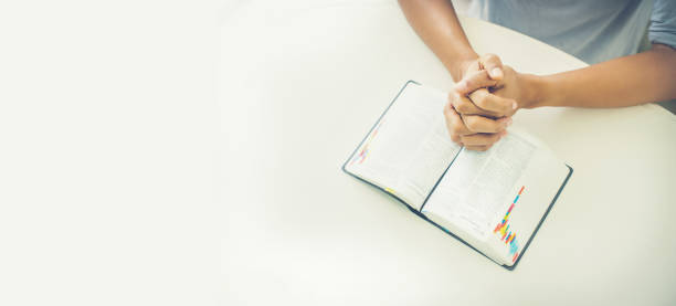 istock Woman hands closed in prayer on an open bible 1300019799