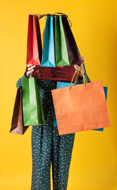woman in green pants holding gift box and multicolored shopping bags on yellow background - fashion fashion model asian ethnicity tall imagens e fotografias de stock