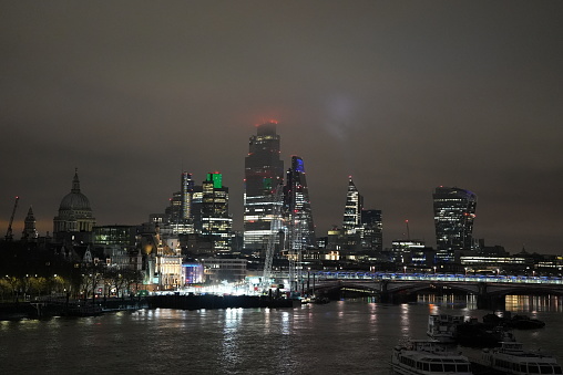 City of London skyline at night in the mist. From the Southbank of the Thames, it shows the City's iconic skyscrapers lit up.