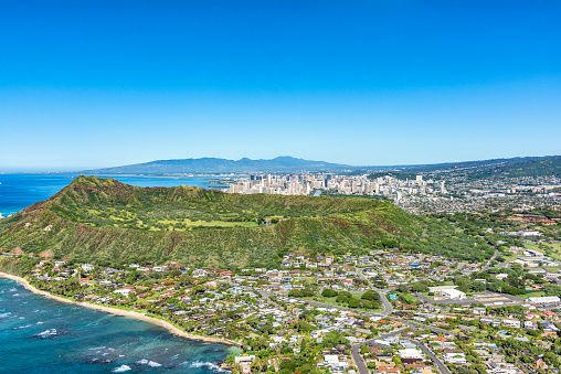 Wide angle aerial view of the majestic Diamond Head volcanic crater towering over the suburbs of Honolulu, Hawaii with its skyline in the distance.