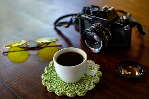 Goiania, Goias, Brazil – February 02, 2021: Old camera, glasses with yellow lenses and cup of coffee on a wooden table.