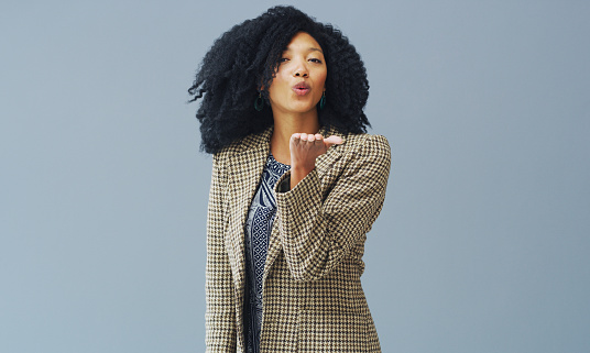 Studio portrait of a young woman blowing a kiss against a grey background