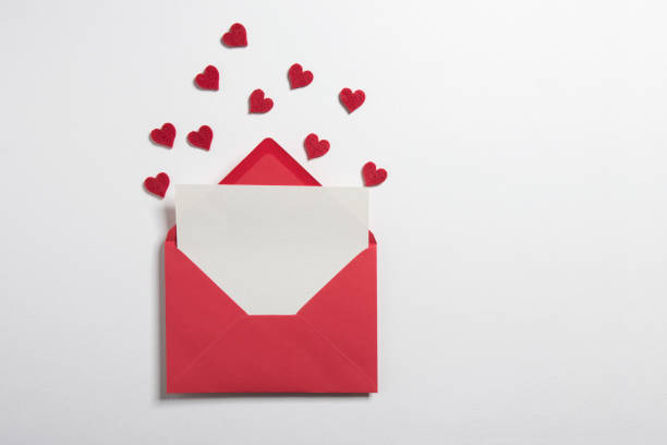 Red paper envelope with blank white note mockup inside and Valentines hearts on white background. Flat lay, top view. Romantic love letter for Valentine's day concept.