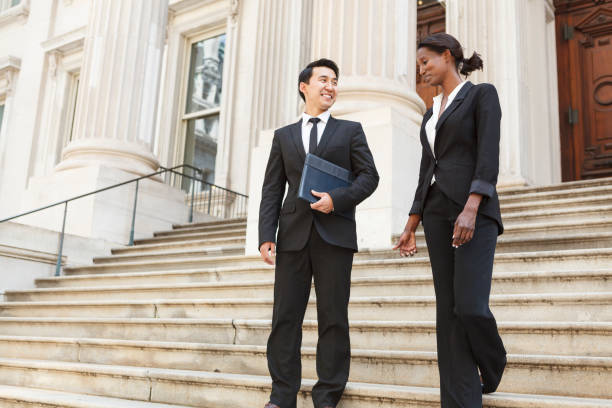 Two Well Dressed Professionals Walk Down Courthouse Steps Outdoors A well dressed man and woman smiling as they as they walk down steps of a courthouse  building. Could be business or legal professionals. lawyer stock pictures, royalty-free photos & images