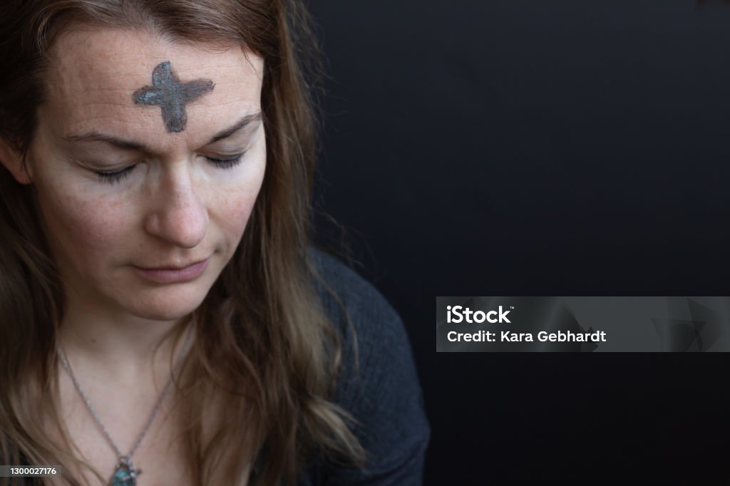 Woman with ash cross on forehead Caucasian woman with ash cross on forehead for Ash Wednesday looking down with eyes closed with black background and copy space Ash Wednesday Stock Photo