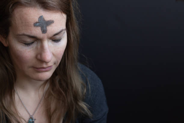 Woman with ash cross on forehead Caucasian woman with ash cross on forehead for Ash Wednesday looking down with eyes closed with black background and copy space ash stock pictures, royalty-free photos & images