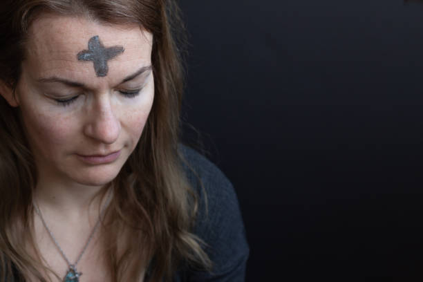 Woman with ash cross on forehead Caucasian woman with ash cross on forehead for Ash Wednesday looking down with eyes closed with black background and copy space ash wednesday stock pictures, royalty-free photos & images