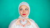 Beautiful young Muslim woman in white  gives a symbol of the heart with her hands. Concept of love, Valentine's Day.